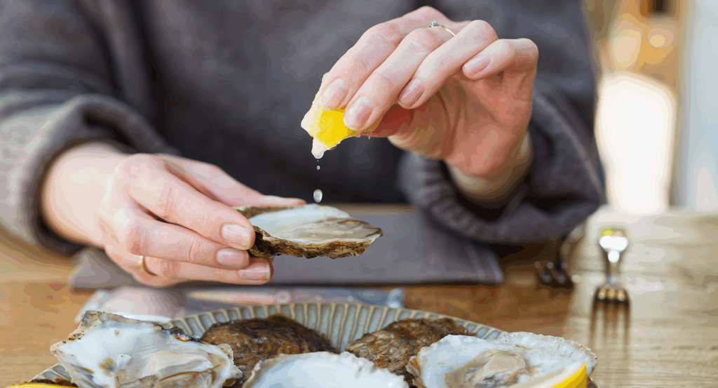 Squeezing a lemon onto a fresh oyster at the best restaurants Malibu has to offer