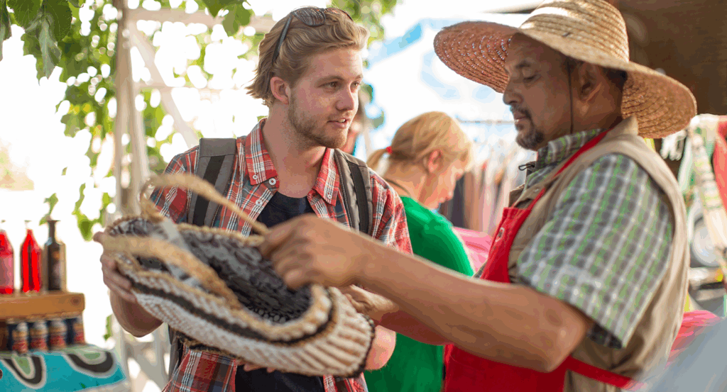 An artisan selling a handmade bag to a man at a Malibu farmers market.