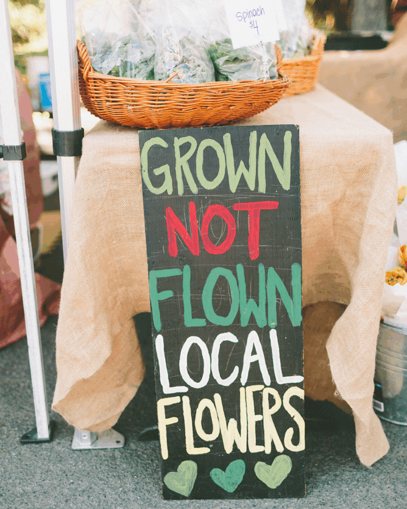 Sign saying Grown Not Flown Local Flowers with a basket of spinach.