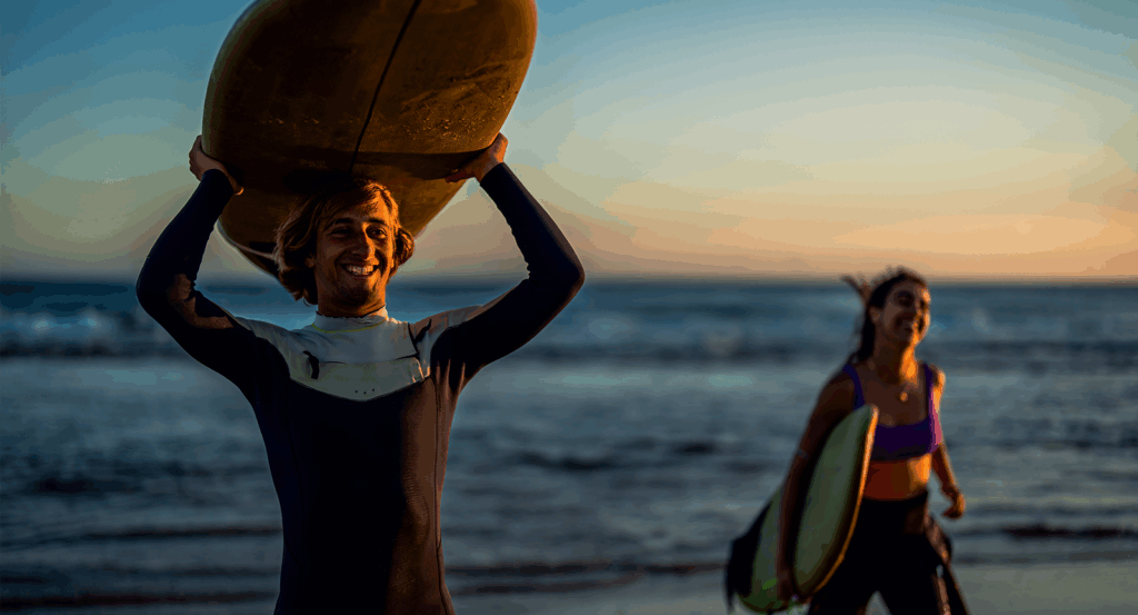 Two Malibu surfing enthusiasts coming out of the water holding surfboards.