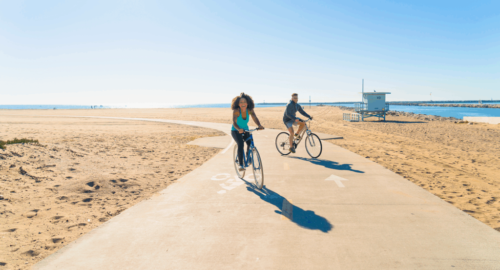 Two people on beach cruisers biking along a beach path in Malibu.
