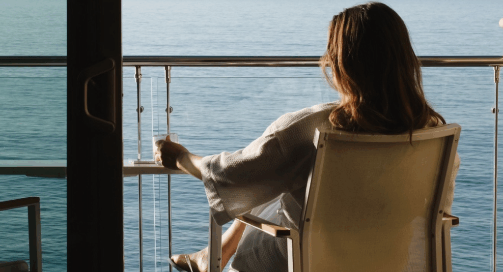 A woman on the balcony of a suite at Malibu Beach Inn sipping coffee overlooking the ocean.