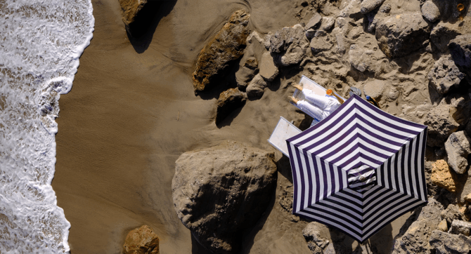 Overhead view of a blue striped umbrella on a beach in Malibu